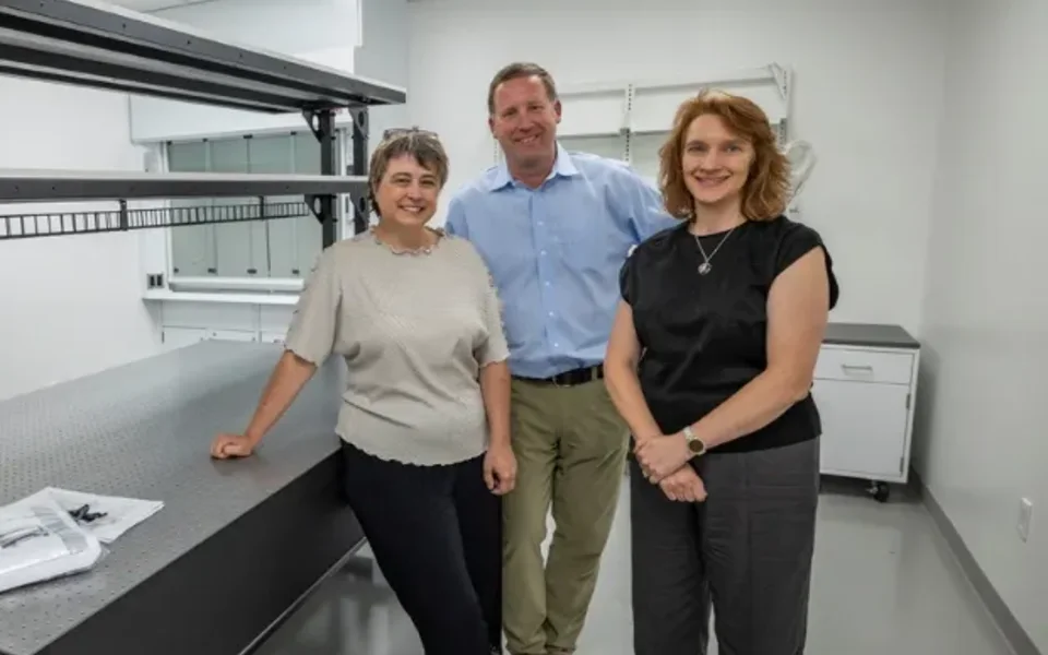 Tanya Ramond, MBA, PhD with two colleagues beside an optical table in a quantum lab at the Colorado Quantum Incubator.