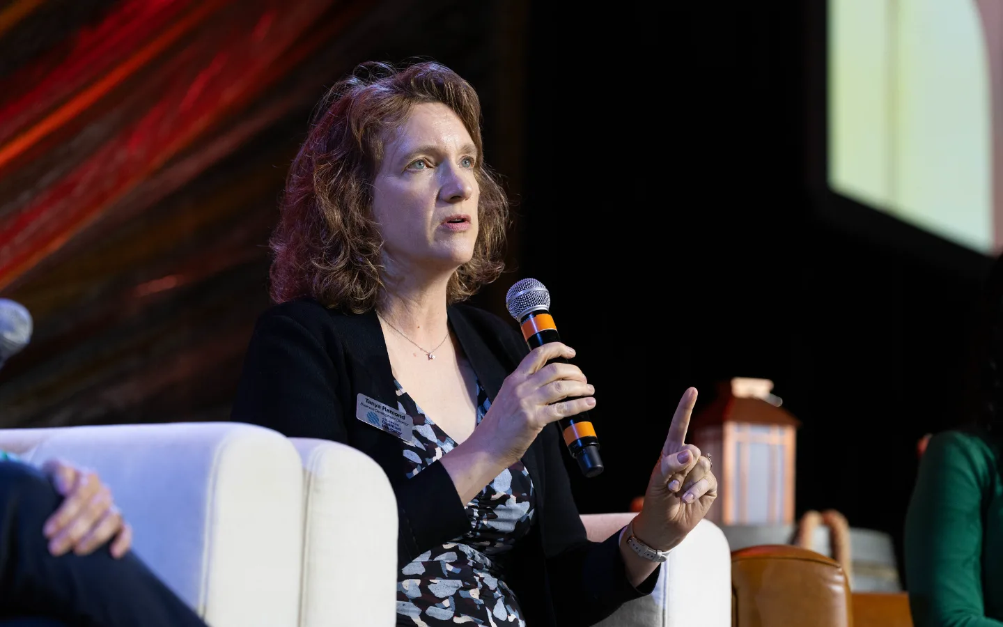 Tanya Ramond, MBA, PhD speaking into a microphone while seated on a panel stage.