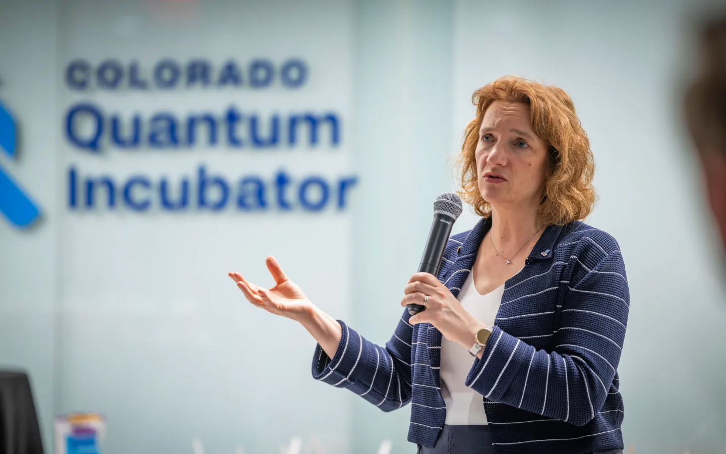 Tanya Ramond, MBA, PhD addressing an audience in front of Colorado Quantum Incubator signage.